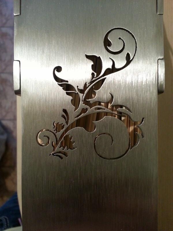 Szczotkowana stal nierdzewna z wycinanym laserowo motywem roślinnym, widoczne zawiasy.