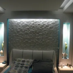 Sypialnia z dekoracyjną ścianą z imitacji cegły, podświetlanymi niszami i białym zagłówkiem łóżka.