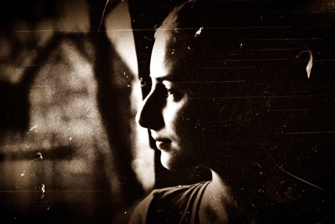 Sepia portret kobiety w ciąży, profil, delikatne oświetlenie z boku, stylizowane na stare zdjęcie z widocznymi rysami i ziarnem.