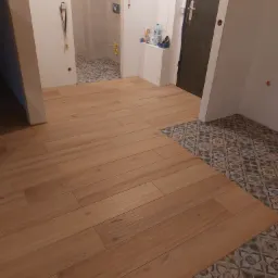 Ułożona podłoga z paneli drewnopodobnych przechodząca w dekoracyjną, wzorzystą terakotę w przedpokoju i łazience w trakcie remontu.