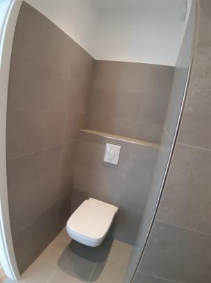 Nowoczesna toaleta podwieszana z szarą glazurą i ukrytym stelażem, widoczny przycisk spłukiwania, minimalizm.