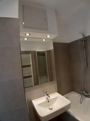 Wykończona łazienka w Widuchowej z umywalką, baterią, lustrem i grzejnikiem drabinkowym, widoczne szare płytki i oświetlenie punktowe.