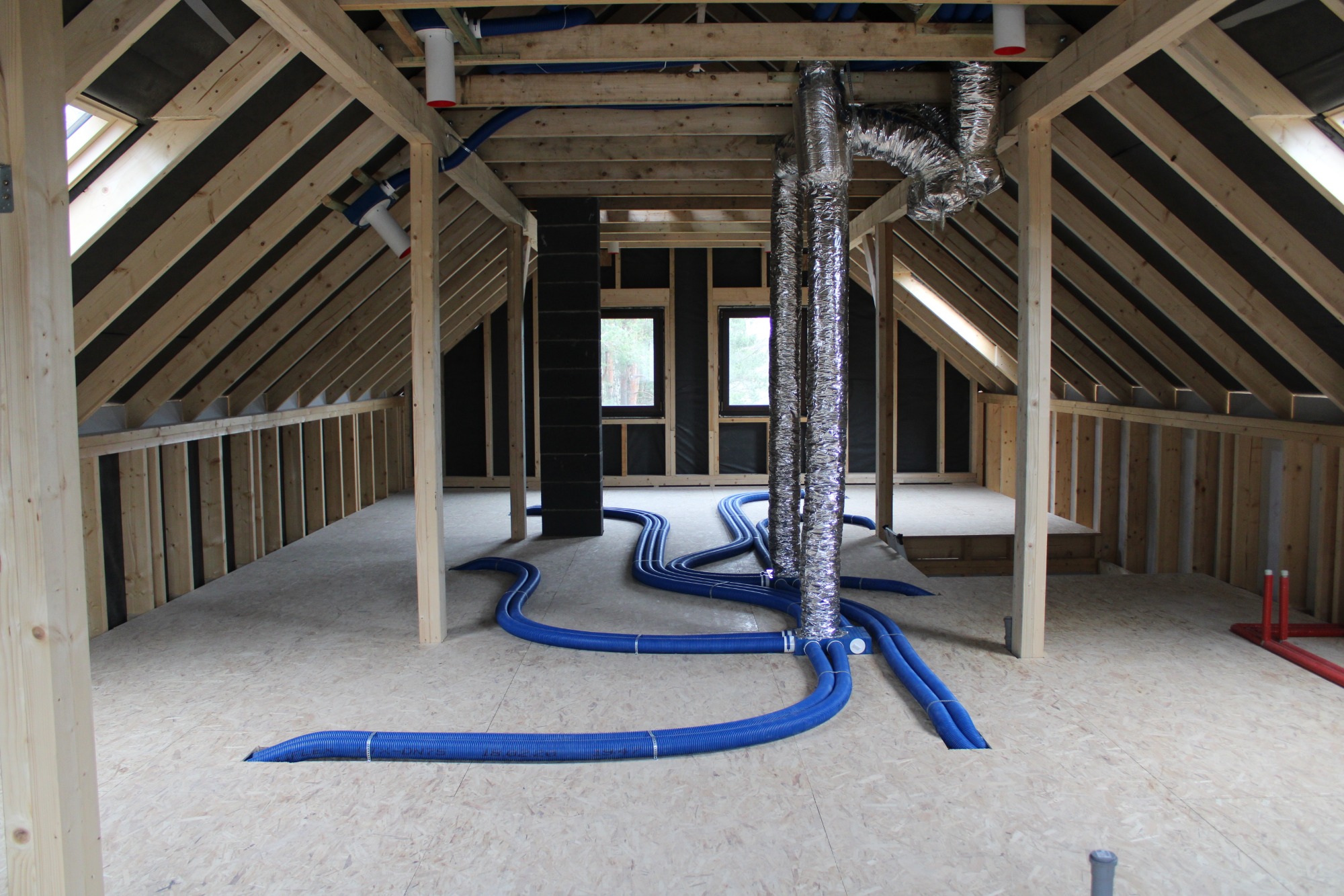 Poddasze w trakcie montażu instalacji rekuperacji: widoczne niebieskie przewody wentylacyjne ułożone na podłodze oraz srebrne, elastyczne rury wentylacyjne prowadzące do dachu.