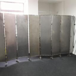 NRS Usługi budowlane Paweł Naras - Składany, metalowy parawan z siedmioma segmentami na kółkach, ustawiony w jasnym pomieszczeniu z oknem.