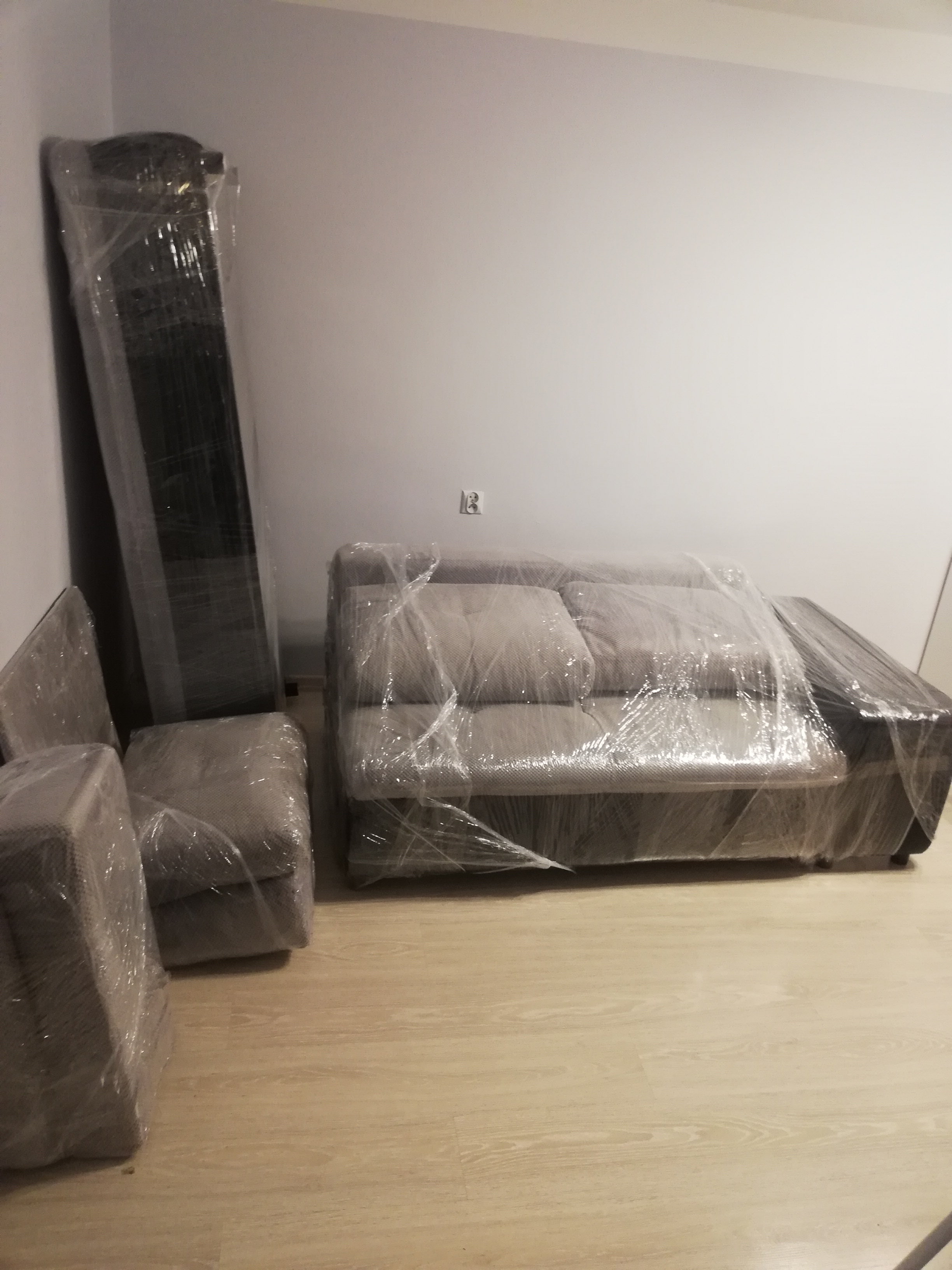 Meble zabezpieczone folią stretch przygotowane do transportu w pustym pomieszczeniu z jasną podłogą.