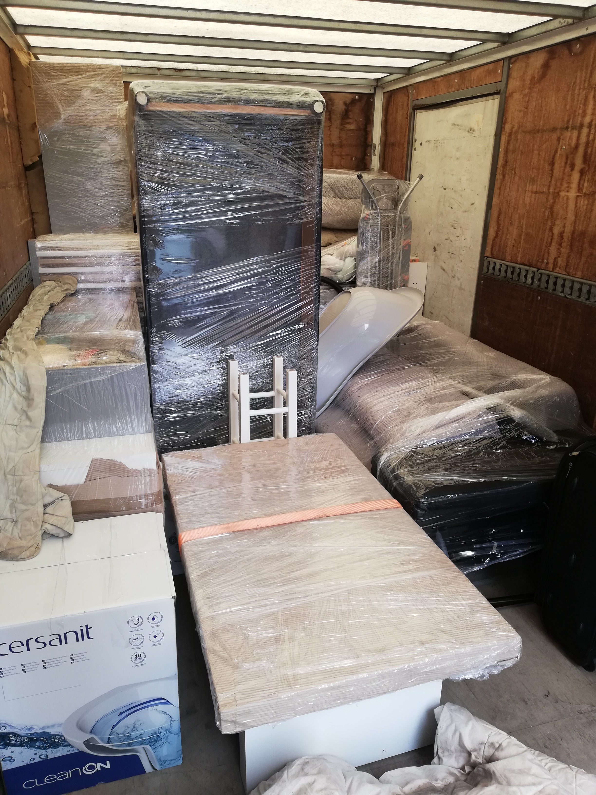 Wnętrze samochodu dostawczego załadowanego meblami i kartonami zabezpieczonymi folią stretch, gotowymi do transportu.