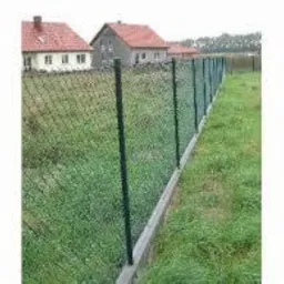 Zielona siatka ogrodzeniowa rozpięta na ciemnych słupkach, widoczna na tle trawy i zabudowań mieszkalnych.