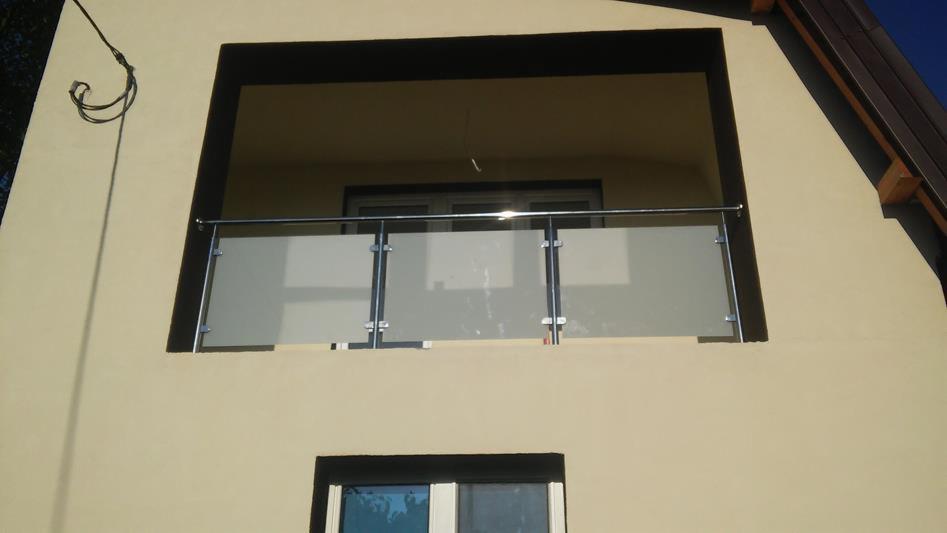 Balkon z mleczną szybą i metalową poręczą, widok z dołu na elewację budynku w jasnym kolorze.