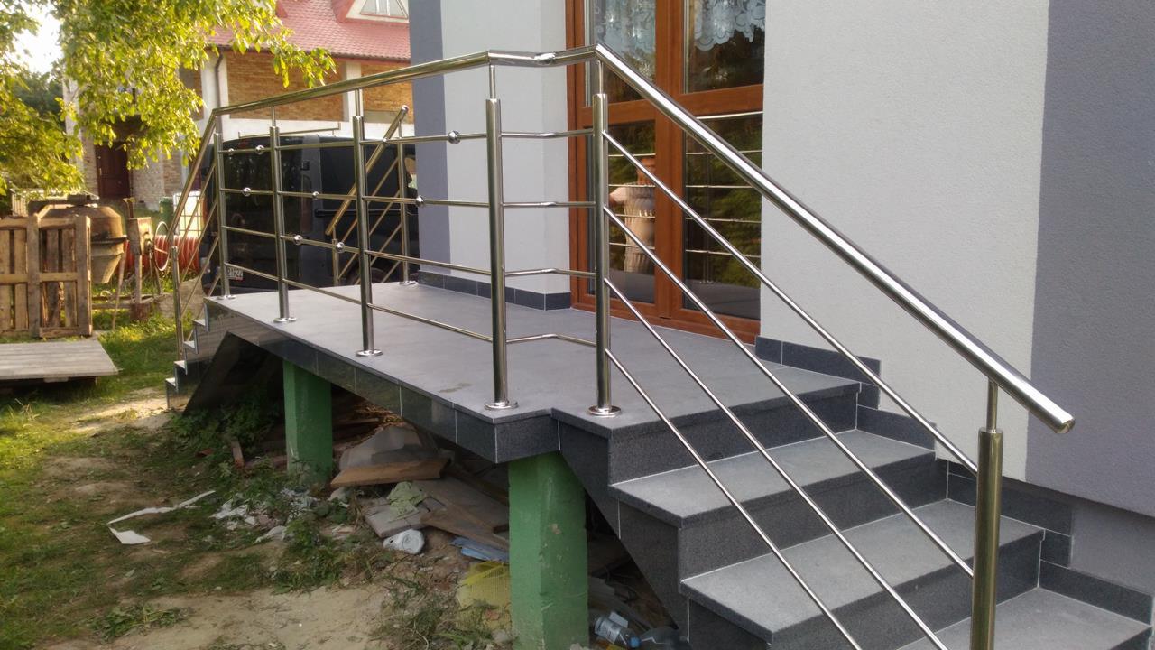 Zewnętrzne schody z szarych płytek z balustradą ze stali nierdzewnej o minimalistycznym designie, widok na dom i otoczenie w tle.