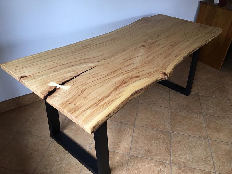 Blat z jasnego drewna z naturalną krawędzią, wzmocniony motylkowym wkładem, osadzony na czarnych, metalowych nogach o kwadratowym przekroju.