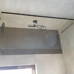 Szklana kabina prysznicowa typu walk-in z czarnymi elementami wykończeniowymi, widoczna armatura, odpływ liniowy i heksagonalne płytki na ścianie.