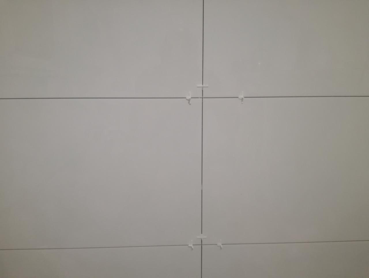 Świeżo ułożone, jasnoszare płytki z białymi krzyżykami dystansowymi, widoczne fugi.