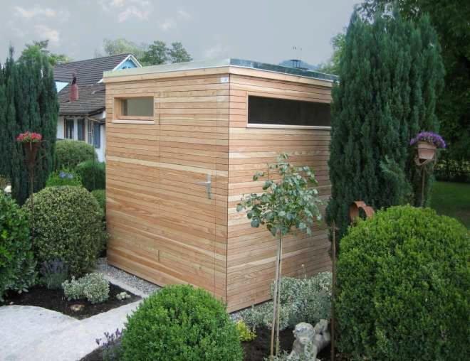 Nowoczesna, drewniana konstrukcja ogrodowa z płaskim dachem i oknami, otoczona bujną zielenią i ścieżką z kamieni.