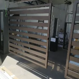 Metalowa balustrada z poziomymi szczeblami w trakcie malowania proszkowego, zawieszona na hakach w lakierni, widoczne elementy systemu transportowego.