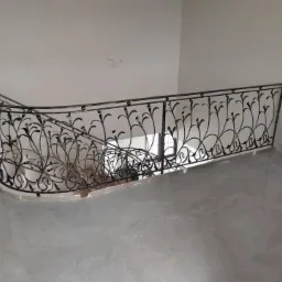 Kuta balustrada schodowa z motywem roślinnym, czarna, z delikatnymi złotymi akcentami, zamontowana na schodach z jasnymi płytkami, widok z góry.