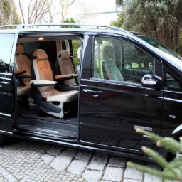 Czarny van z otwartymi drzwiami, ukazujący jasne skórzane fotele z podłokietnikami, zaparkowany na brukowanej drodze, z widocznym logo 'V6' na błotniku.