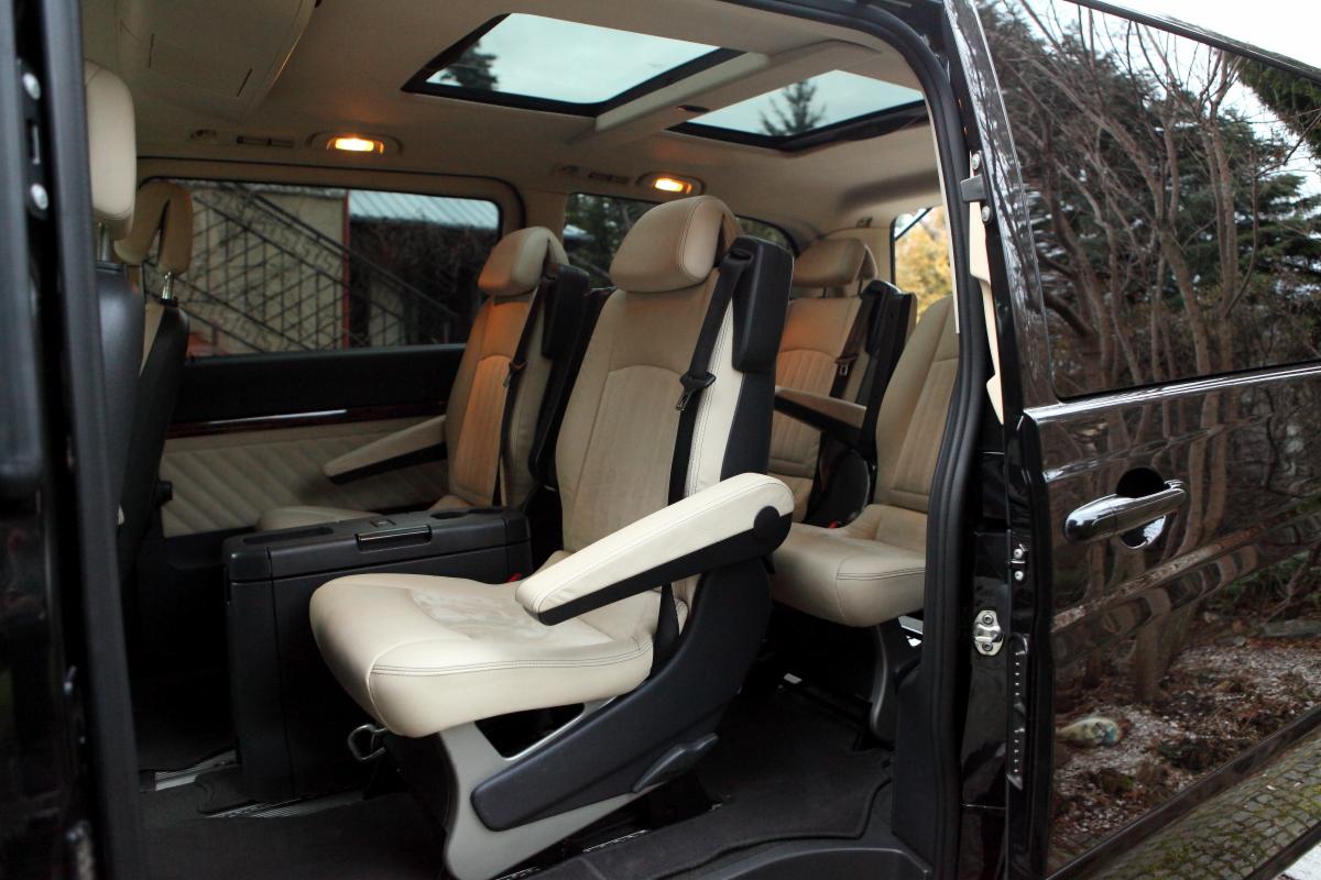 Wnętrze luksusowego vana z beżową skórzaną tapicerką, widok z otwartych drzwi na przestronne siedzenia i panoramiczny dach.