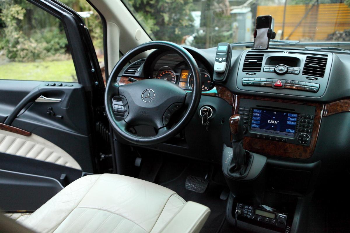 Wnętrze samochodu Mercedes Vito z jasną skórzaną tapicerką, widoczny kokpit z radiem i kierownica z logo Mercedes-Benz, kluczyki w stacyjce i uchwyt na telefon na desce rozdzielczej.