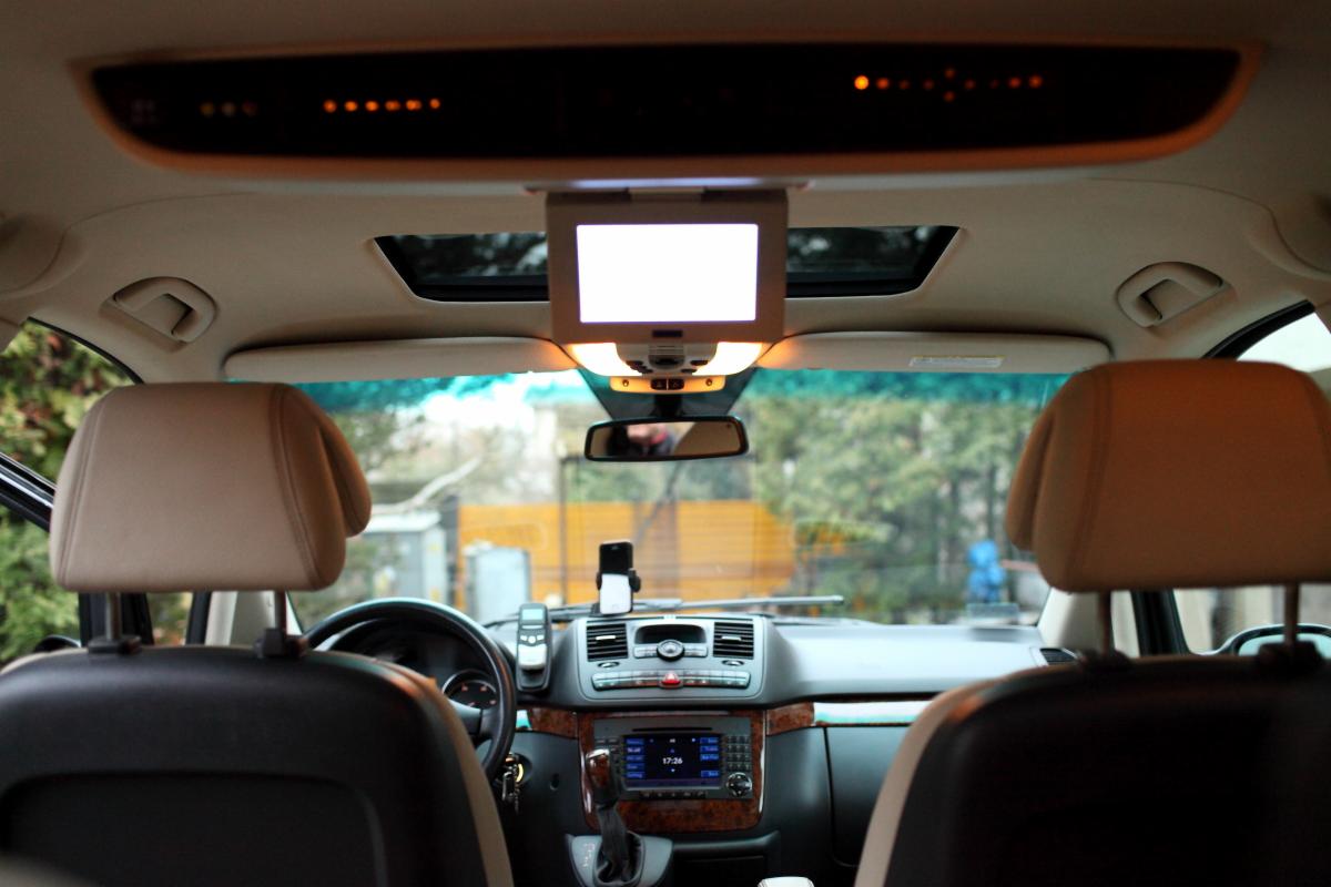 Wnętrze samochodu z zamontowanym ekranem dla pasażerów z tyłu, widok z tylnych siedzeń na deskę rozdzielczą i otwarty szyberdach.