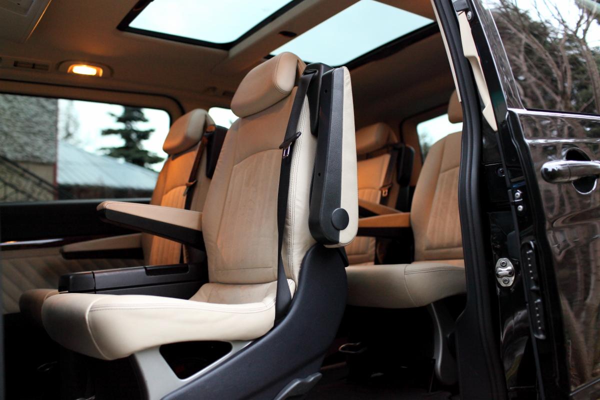 Wnętrze luksusowego busa z beżowymi skórzanymi fotelami, widoczne otwarte drzwi i panoramiczny dach.