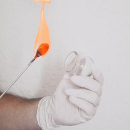 Gabinet Masażu i Chiropraktyki - Szklana bańka do masażu ogniowego ogrzewana płomieniem, trzymana w dłoni w białej rękawiczce na tle białego prześcieradła.