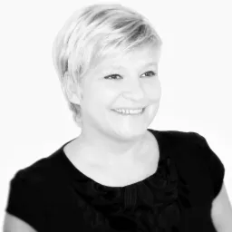 Portret uśmiechniętej blondynki w czarnej bluzce na jasnym tle, w czerni i bieli. Zdjęcie biznesowe, budzące zaufanie.