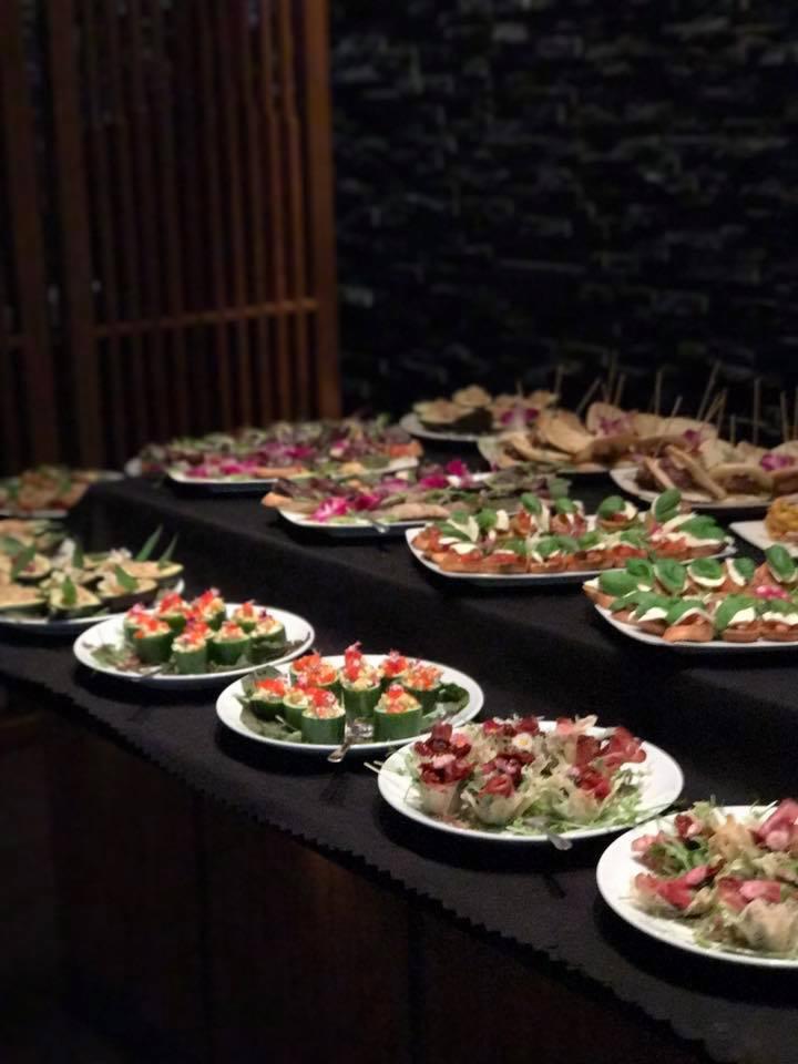 Elegancko zastawiony stół z różnorodnymi przekąskami na białych talerzach, w tym ogórki faszerowane czerwonym kawiorem, mini kanapeczki z pomidorami i bazylią, oraz sałatki w kruchych koszyczkach...