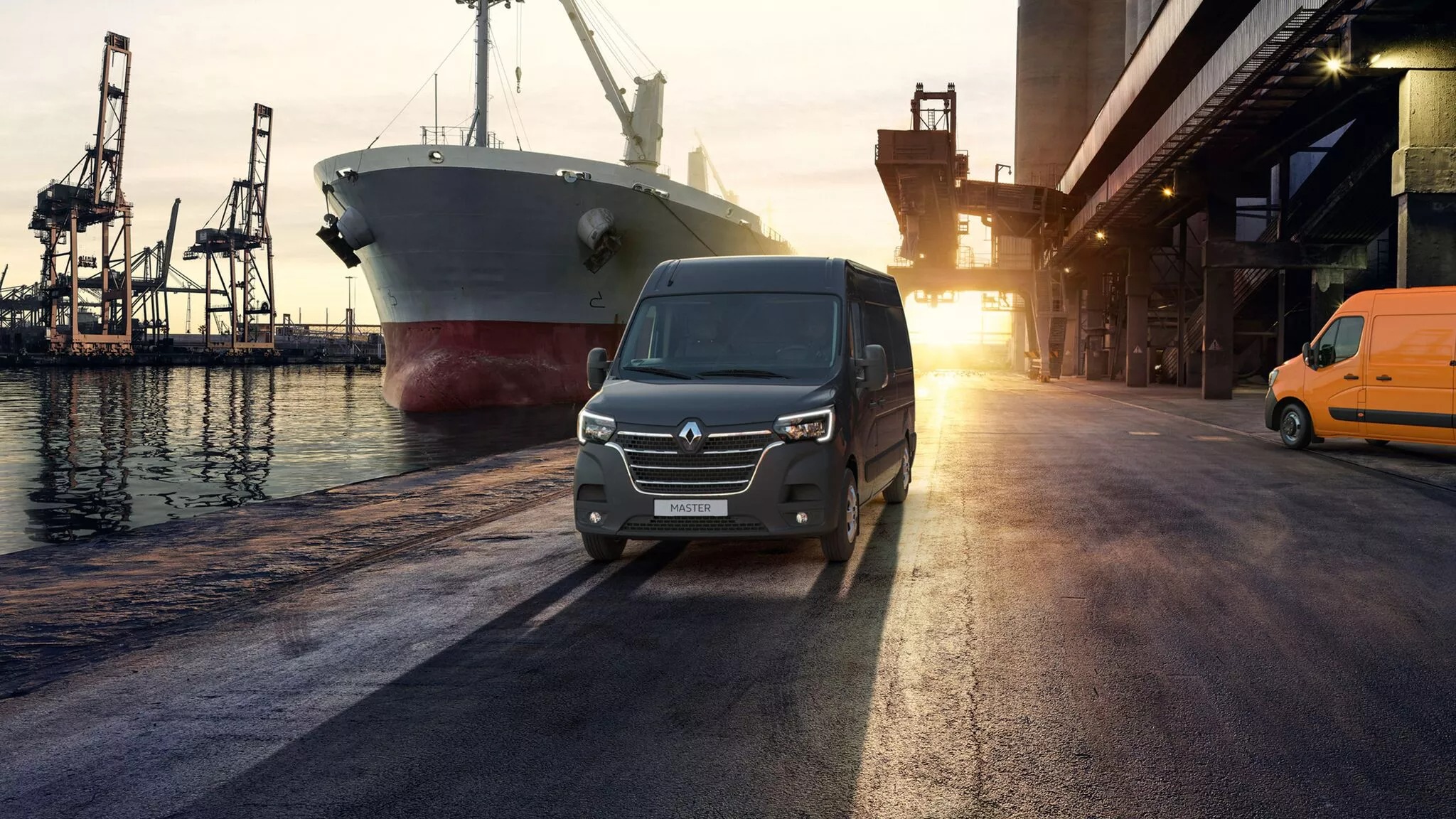 Czarny Renault Master na tle portu z dużym statkiem towarowym i dźwigami, obok stoi pomarańczowy bus.
