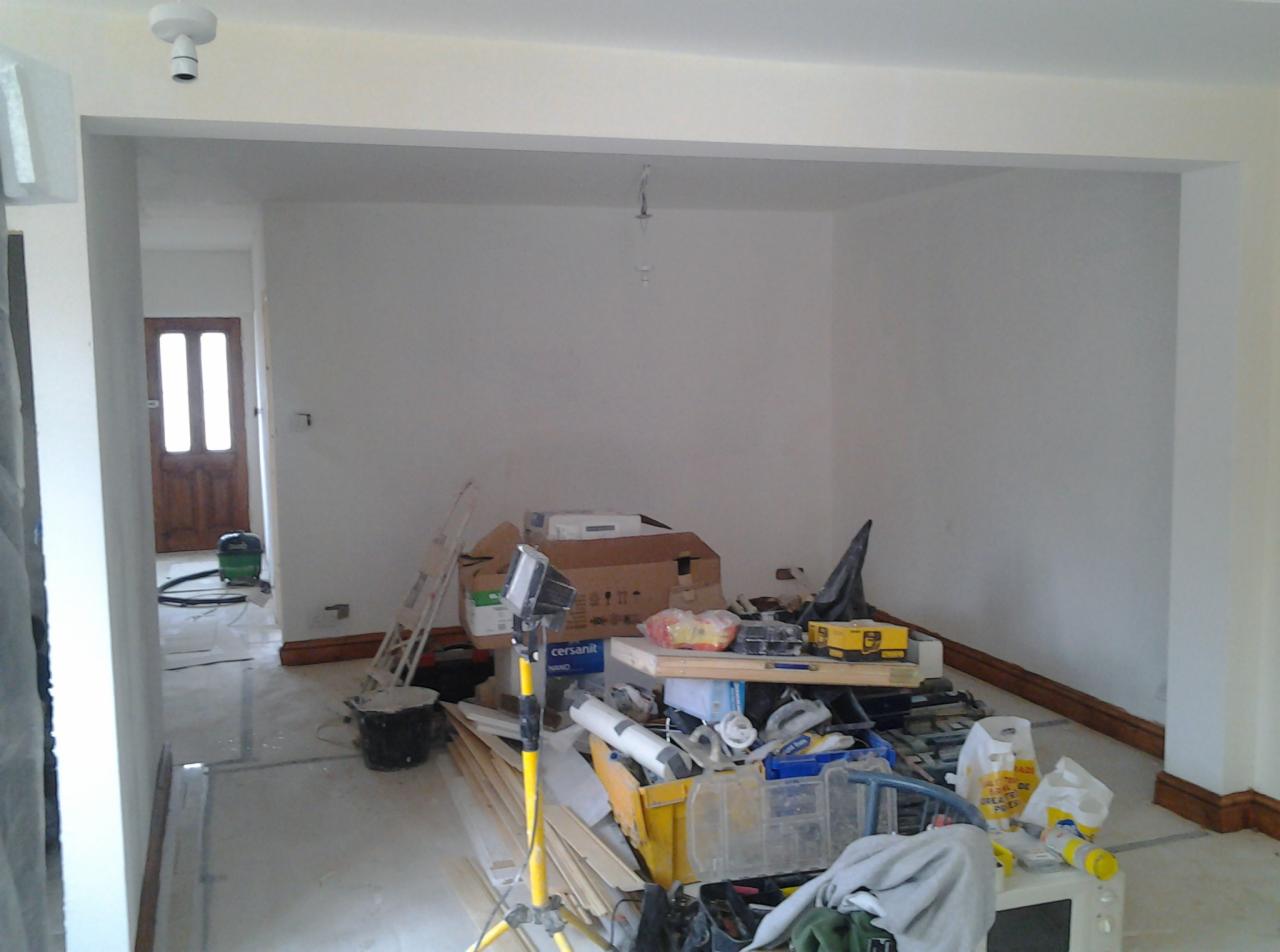 Wnętrze w trakcie prac wykończeniowych w Sztutowie, widoczny bałagan, drabina, lampa budowlana, przygotowane materiały i narzędzia, ściany w trakcie malowania.