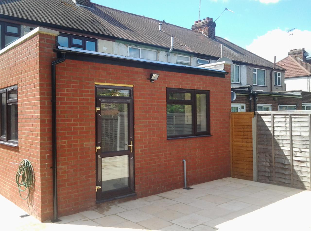 Nowo dobudowana, czerwona, ceglana przybudówka do domu z brązowymi oknami i drzwiami, wyłożona jasną kostką brukową.