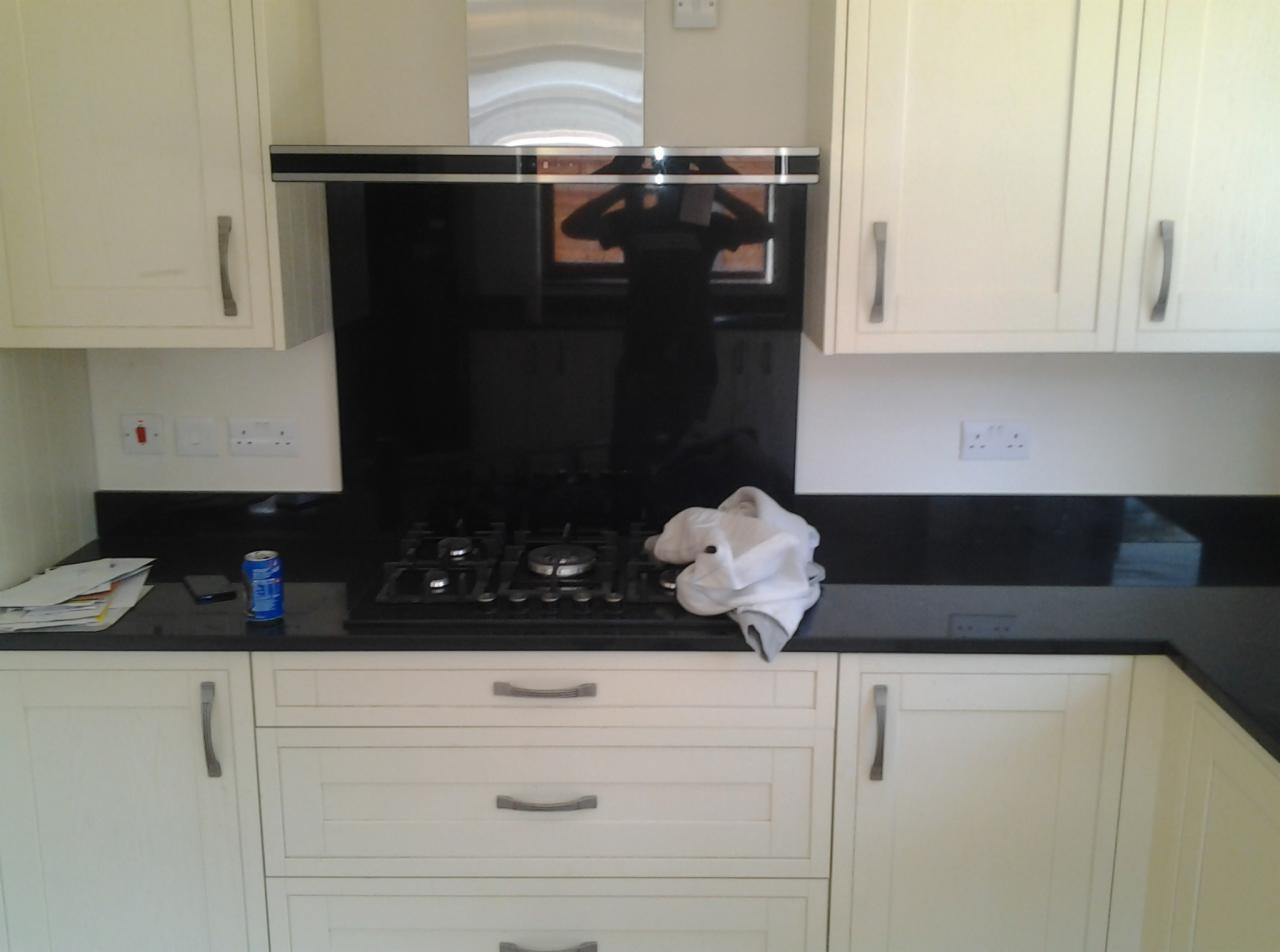 Wykończona kuchnia z kremowymi szafkami, czarnym blatem i panelem nad płytą gazową, na której leży biała ściereczka, odbicie osoby w panelu.