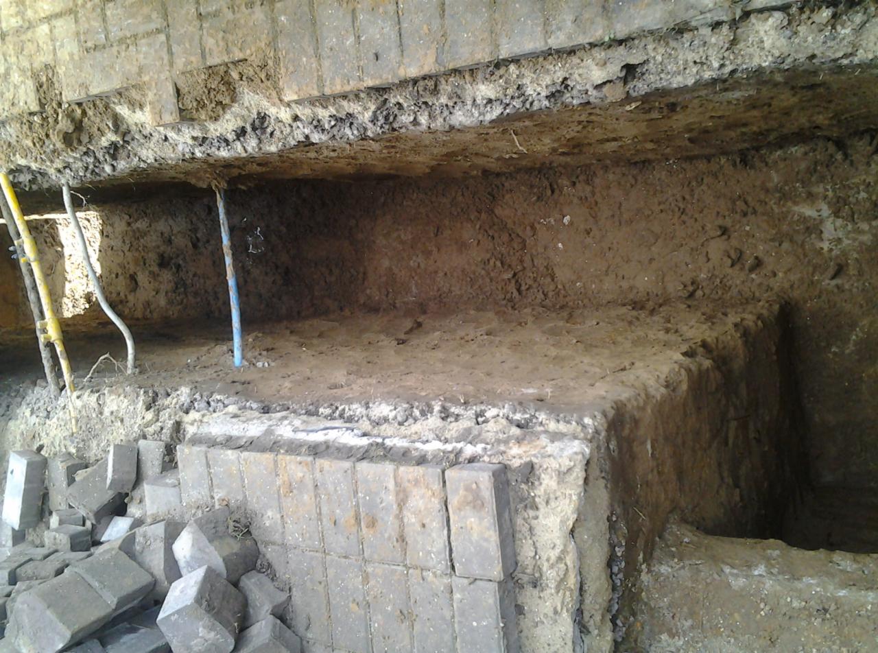 Wykonany wykop pod fundament z częściowo ułożoną kostką brukową na krawędzi, widoczne podpory i ziemia.