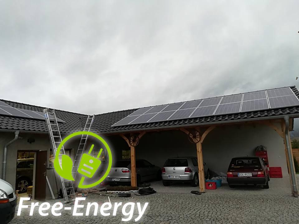 Panele słoneczne zamontowane na dachu garażu z drewnianą konstrukcją, drabina oparta o dach, logo 'Free-Energy' w lewym dolnym rogu.