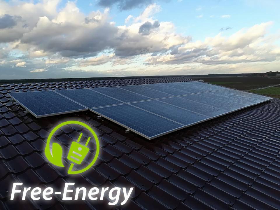 Panel słoneczny na brązowym dachu z dachówki ceramicznej, z zielonym logo 'Free-Energy' na pierwszym planie, pochmurne niebo w tle.