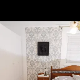 Wzorzysta tapeta w sypialni z drewnianym łóżkiem, szafką nocną i białą szafą wnękową, ozdobiona czarną płaskorzeźbą nad łóżkiem.