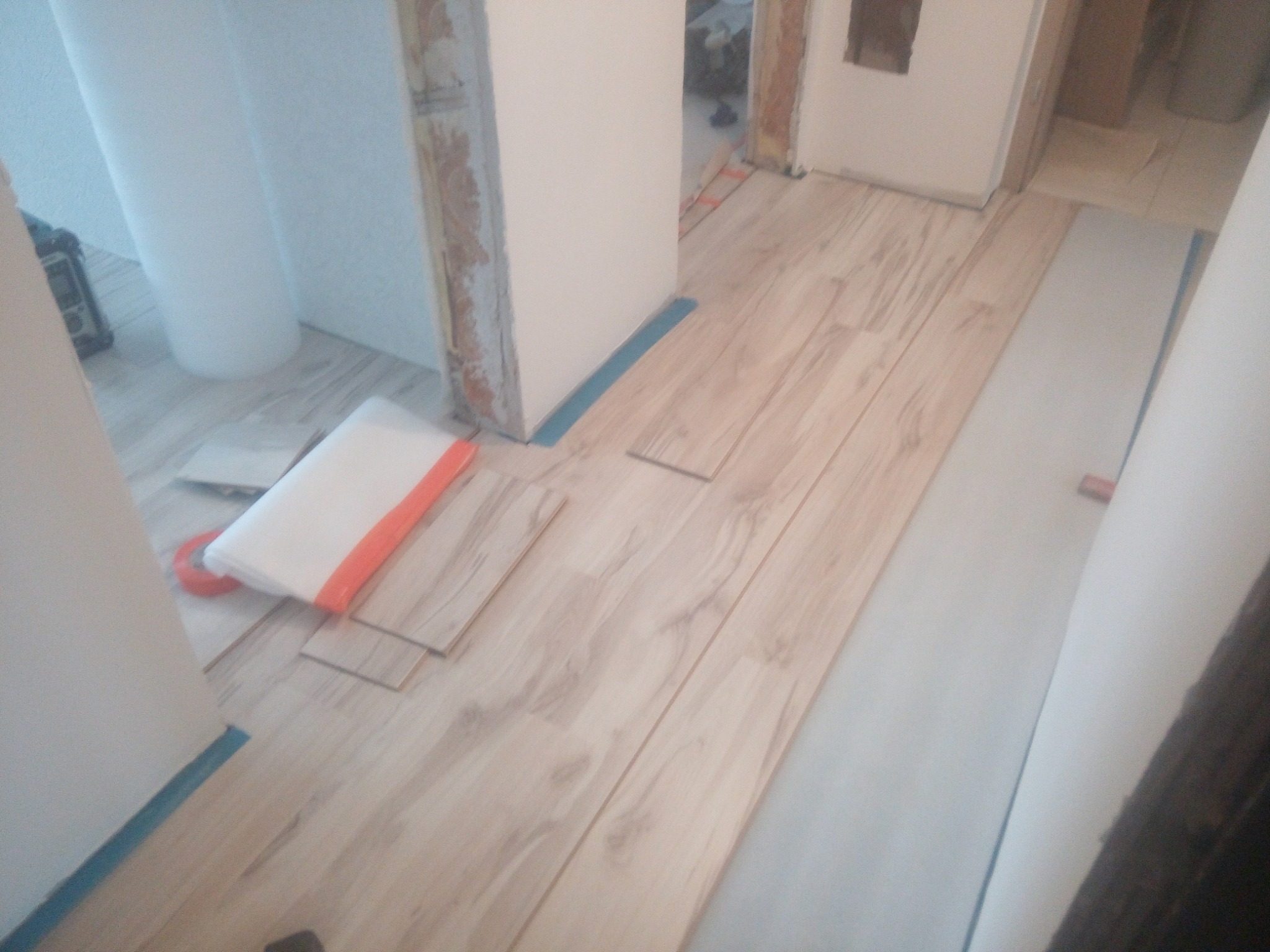 Układanie jasnych paneli podłogowych w trakcie remontu mieszkania, widoczne zabezpieczenia ścian i folia ochronna.