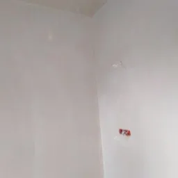 Wnętrze po nałożeniu warstwy gładzi, widoczne ślady szpachlowania i przygotowania do malowania, z wystającymi przewodami elektrycznymi.