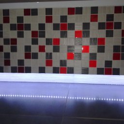 TytusBud - Mozaika z kwadratowych płytek w odcieniach szarości, bieli i czerwieni, podświetlona listwą LED. Nowoczesny design, precyzyjne ułożenie, błyszcząca powierzchnia.