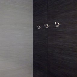 TytusBud - Wykończona ściana łazienki z szarymi i ciemnymi płytkami imitującymi drewno, z trzema chromowanymi haczykami na ręczniki. Widoczny fragment narożnika.