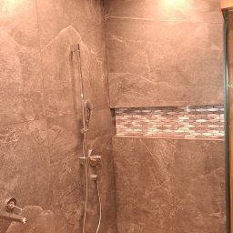 TytusBud - Wykończona kabina prysznicowa z szarymi płytkami imitującymi kamień i dekoracyjną wnęką z mozaiką. Chromowana armatura i odpływ liniowy.