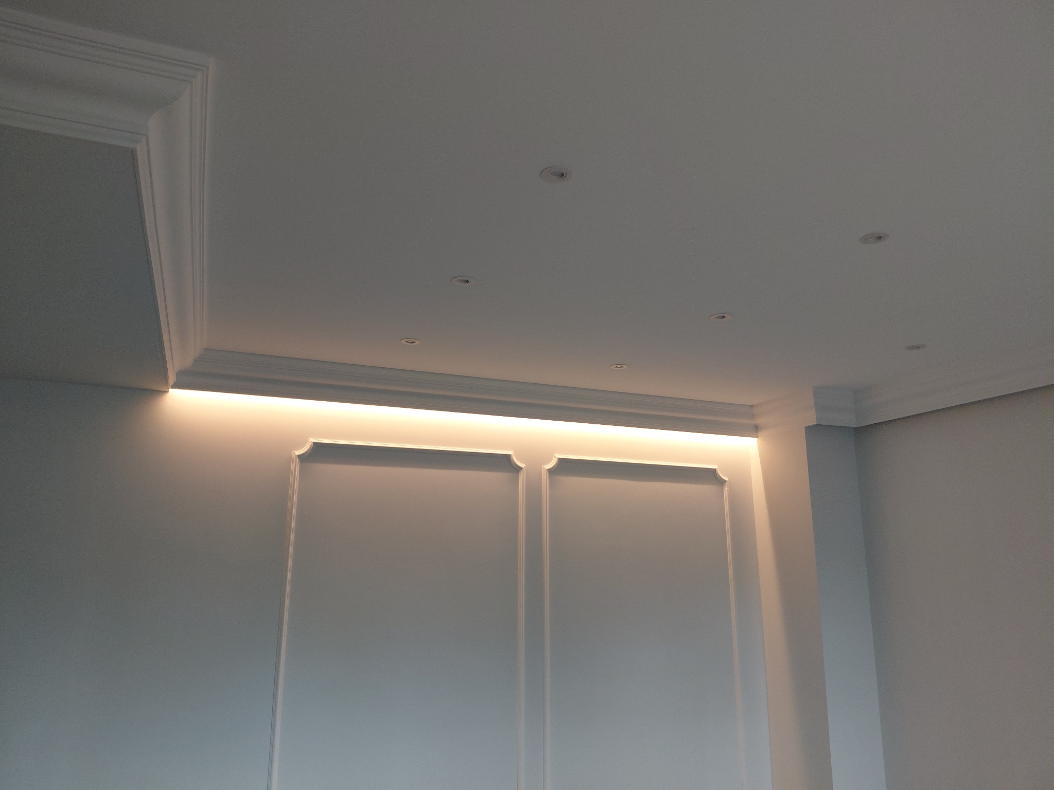 Białe ściany z dekoracyjnymi panelami i oświetleniem LED w suficie, wykończenie wnętrza w minimalistycznym stylu z elementami klasycznymi.