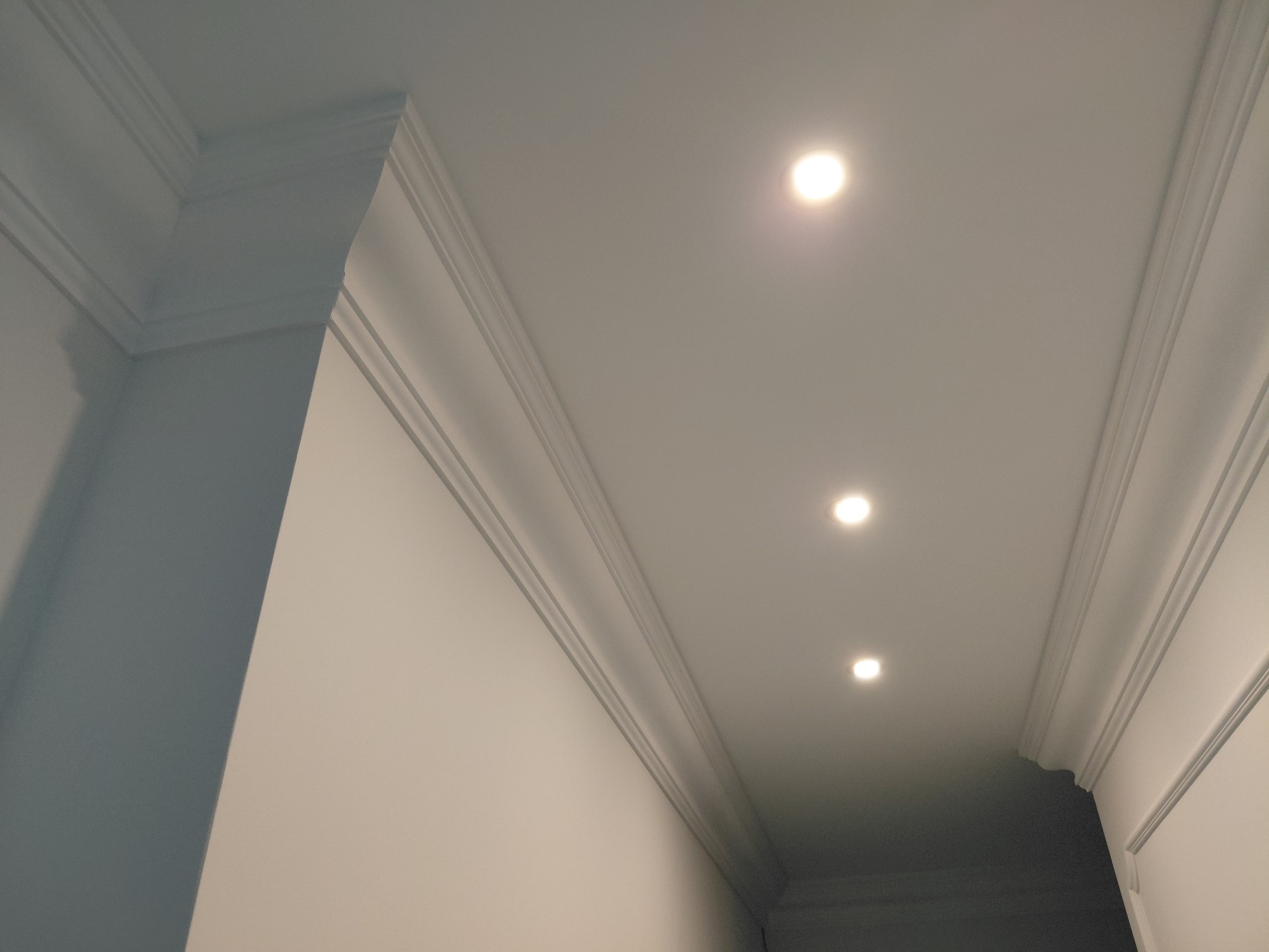 Biały sufit z ozdobną listwą przysufitową i trzema punktowymi lampami LED, widok z dołu, podkreślający detale wykończenia wnętrza.