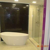 Nowoczesna łazienka z wolnostojącą, owalną wanną na tle ściany wyłożonej czarną mozaiką w kształcie plastra miodu oraz przeszkloną kabiną prysznicową.