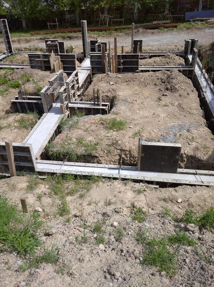 Przygotowanie fundamentów pod budynek: wykopane rowy zalane betonem, szalunki z desek i zbrojenie stalowe, widoczne elementy konstrukcyjne.