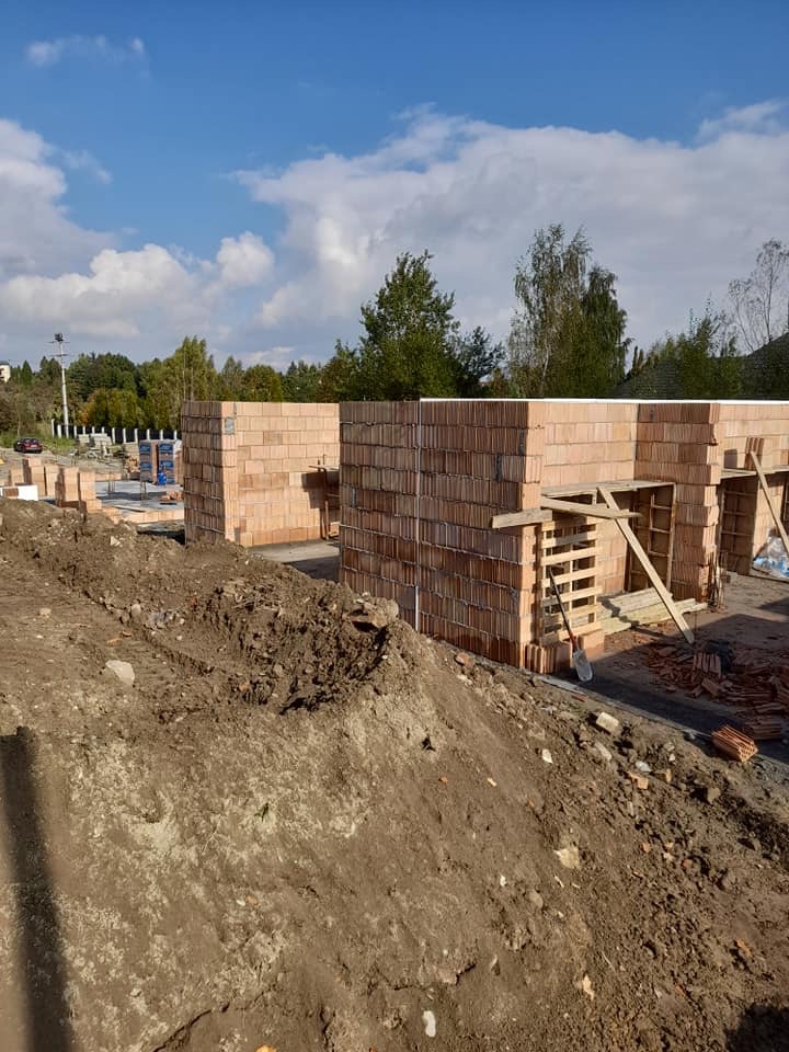 Wznoszenie ścian zewnętrznych budynku z czerwonej cegły ceramicznej Porotherm, widok na plac budowy w słoneczny dzień.