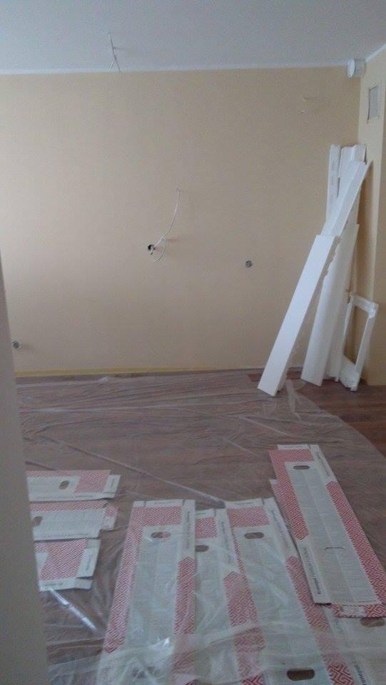 Pokój przygotowany do malowania: podłoga zabezpieczona folią ochronną, listwy przypodłogowe oparte o ścianę, widoczne kable elektryczne wystające ze ściany.