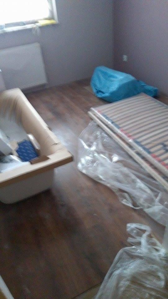 Przygotowania do remontu: stara wanna, zabezpieczone folią elementy i niebieski worek na gruz na podłodze z paneli.