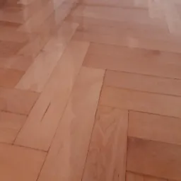 Świeżo polakierowany parkiet ułożony w jodełkę, z widocznymi refleksami światła i drobnymi niedoskonałościami na powierzchni.