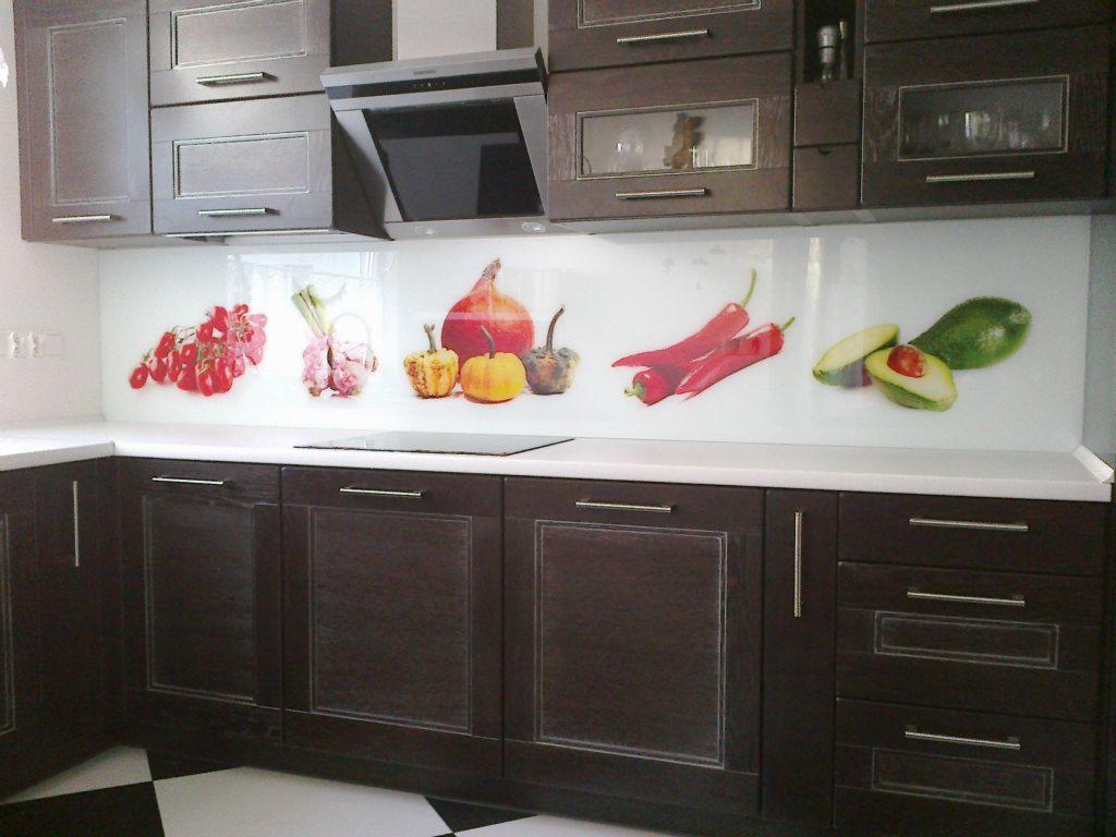 Szklany panel kuchenny z nadrukiem warzyw i owoców, zamontowany nad blatem z ciemnobrązowymi szafkami kuchennymi i czarno-białą podłogą w szachownicę.