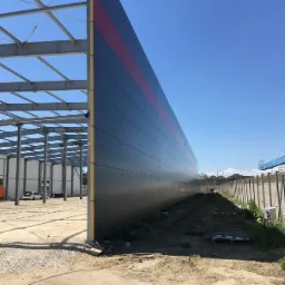 Budowa hali: widok na stalową konstrukcję i ścianę z płyt warstwowych z czerwoną linią, w tle błękitne niebo.